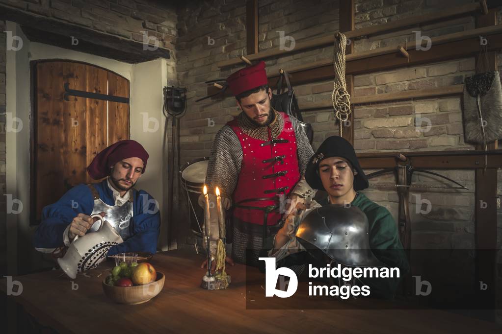 In the guard body, a young man takes care of the captain's helmet. On the left, a man of arms pours a drink, Hypothesis reconstructive uses and customs Middle Ages Italy, Mondaino, Italy (photo)