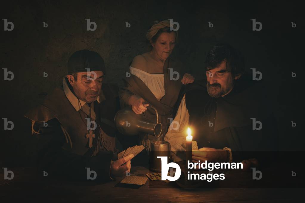 17th century, North Italy: country militia. Reconstructive hypothesis civil and military uses and customs. In the tavern you play cards, while a woman pours a drink, Verrua Savoia, Turin, Piedmont, Italy (photo)