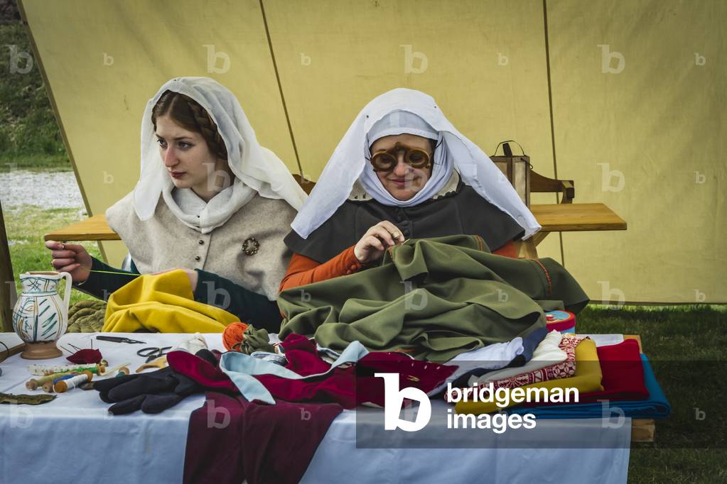 Reconstructive hypothesis of customs and customs, arts and crafts 14th century: Couple of women, performing tailoring work, Villafranca di Verona, Veneto, Italy (photo)