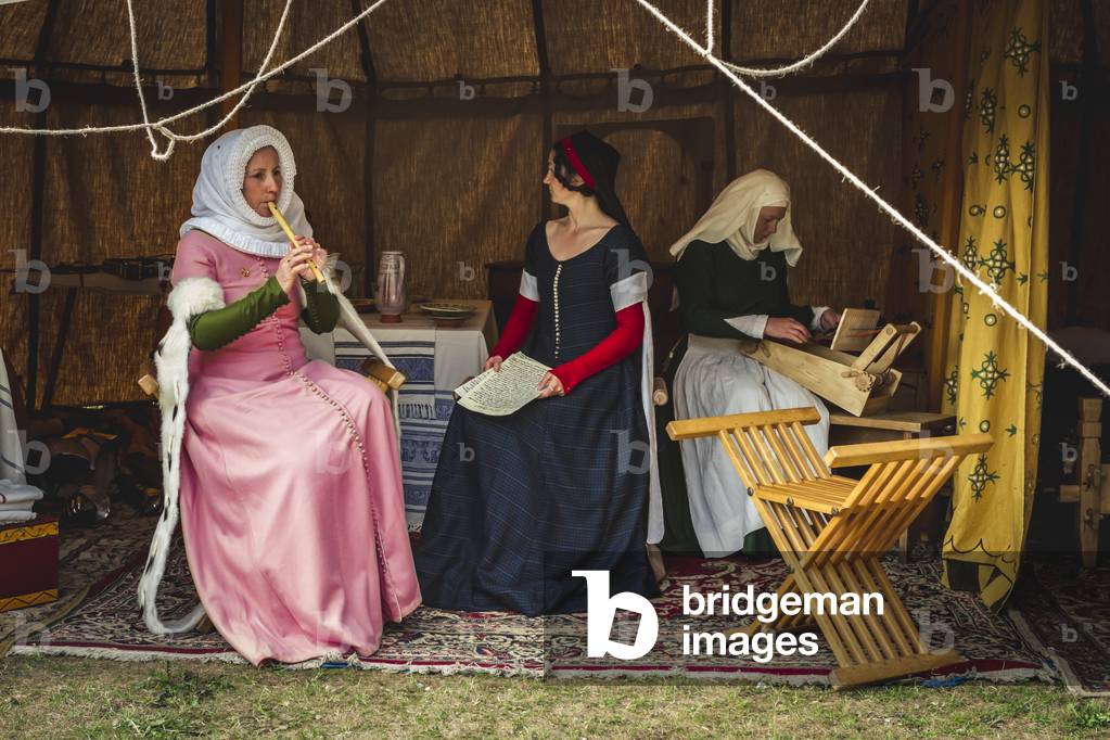 Reconstructive hypotheses of uses and customs, arts and crafts 14th century: Inside a tent, music is made, singing and working on the loom, Villafranca di Verona, Veneto, Italy (photo)