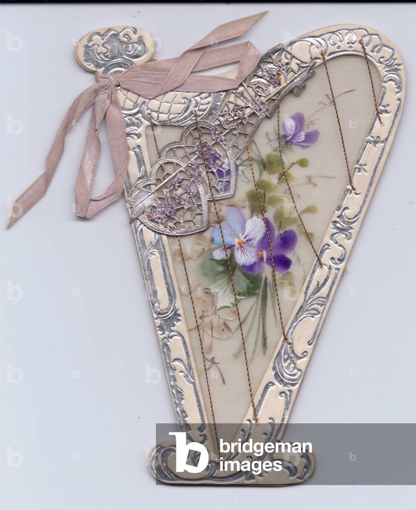 A greeting card made of plastic in the shape of a harp with cord strings, hand-painted flowers and a pink bow, circa 1910 (plastic)