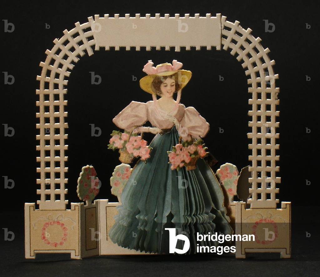 A Victorian die cut honeycomb greeting card of a woman under a lattice archway holding two baskets of flowers, c.1880 (colour litho)