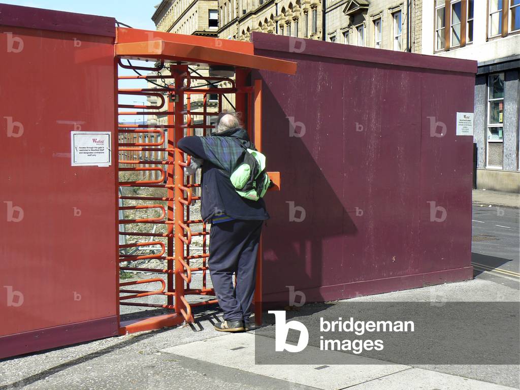 A man leans against a barrier to try to see what is hidden beyond