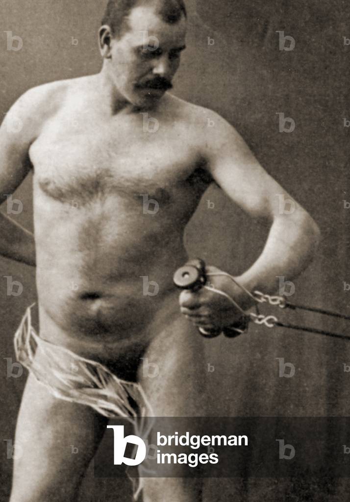Nude male holding the handle of a cable machine, c.1910 (sepia photo)