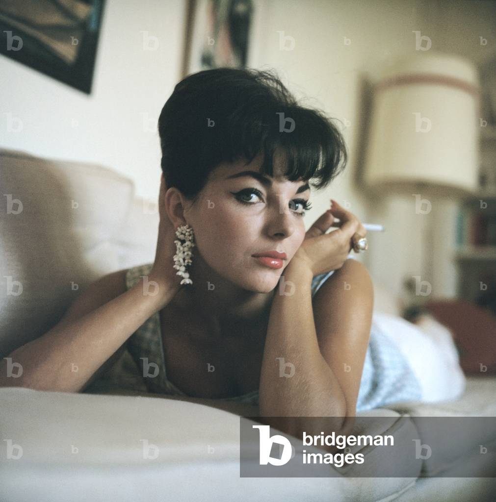 Publicity Handout Photograph Of Actress Joan Collins (B. 1933), On A Couch, Holding A Cigarette Near Her Face, Ca. 1950S.