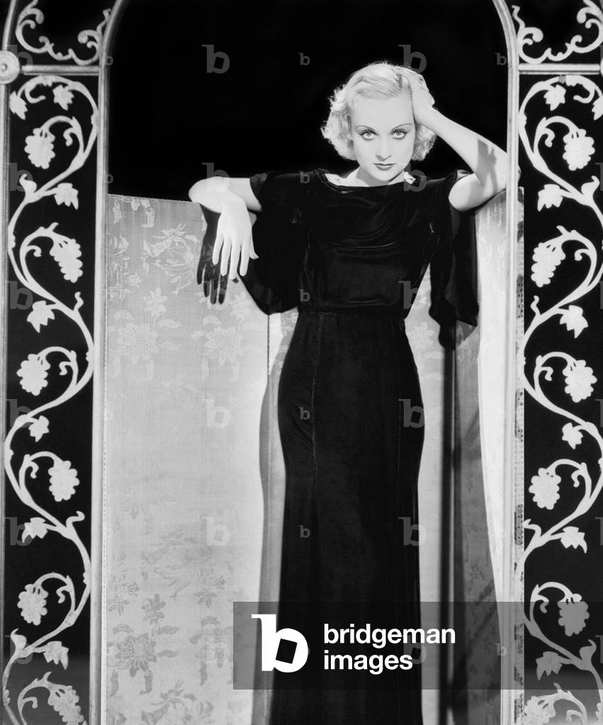 Circa 1930: American Film Actress Carole Lombard (1908 - 1942) Wearing A Full-Length Black Evening Dress And A Velvet Cape.