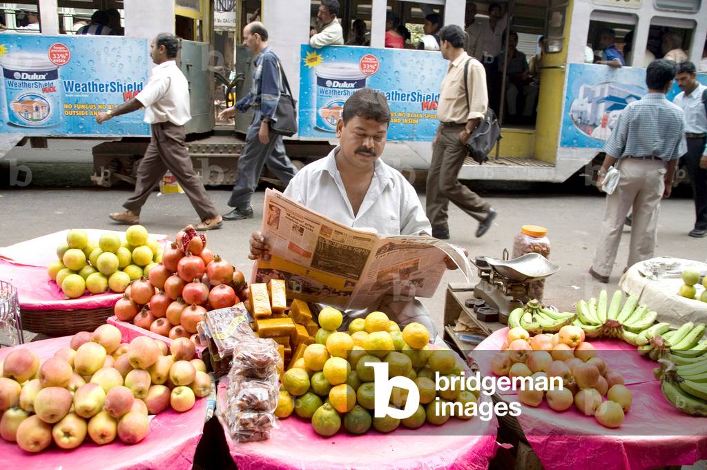 Fruit vendor reading a newspaper, Calcutta now Kolkata, West Bengal, India (photo)
