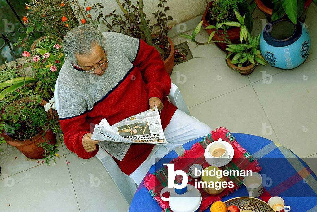 Eighty year old senior citizen enjoying morning tea time, sitting on a terrace and reading a newspaper, Kalyaninagar, Pune, Maharashtra, India (photo)