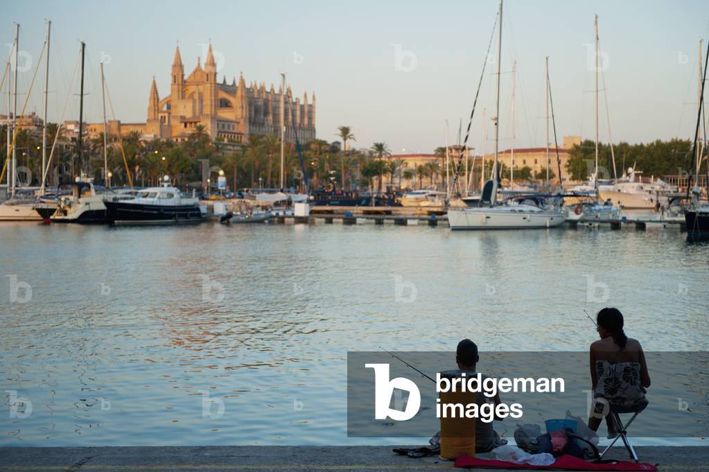 Spain, Majorca, Couple fishing in harbor in front of cathedral at dusk, Palma (photo)