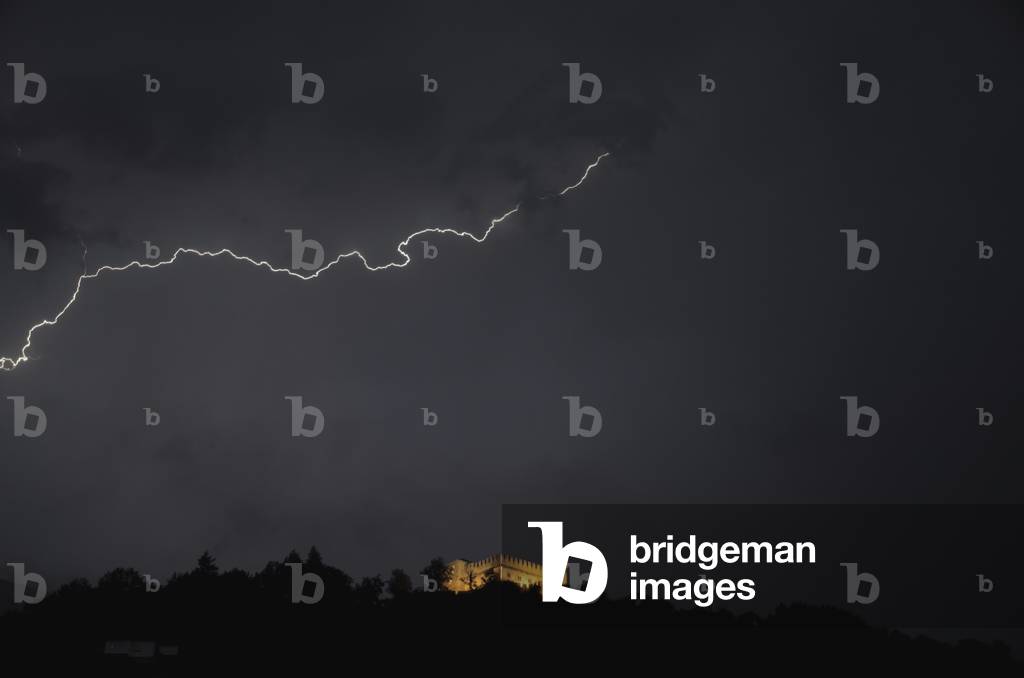Lightning strike in the dark sky and an illuminated castle below, Bellinzona, Ticino, Switzerland (photo)