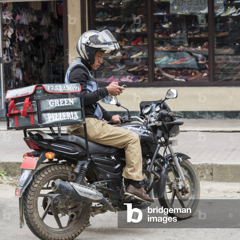 Pizza delivery man on a motorcycle in the street using a smart phone, Thimphu, Bhutan (photo)
