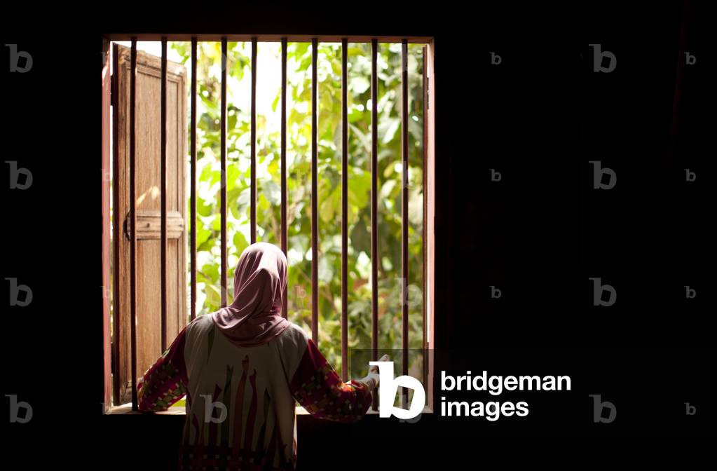 A Woman looking out the Grate Covering a Window, Tanjung Lubuk Sumatera Selatan Indonesia (photo)