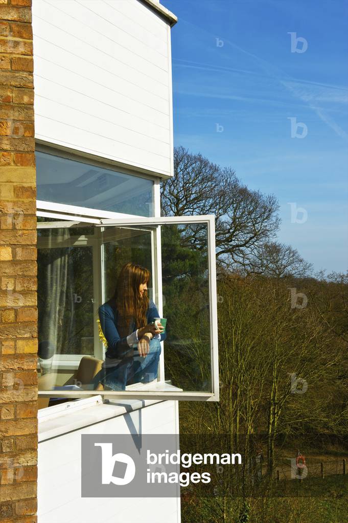 A young woman sits on a window ledge looking out, Hampstead Heath, London, England, UK  (photo)