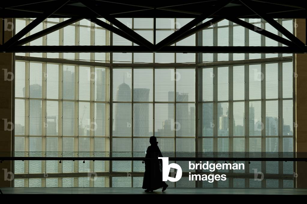 Silhouette of woman walking past large window in the Museum of Islamic Art in front of the modern city skyline of Doha, Doha, Qatar (photo)