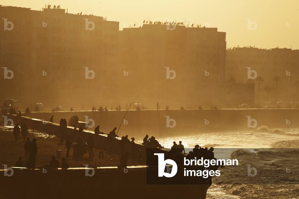 Morocco, People sitting and fishing at dusk from sea wall beside Hassan II Mosque, Casablanca (photo)