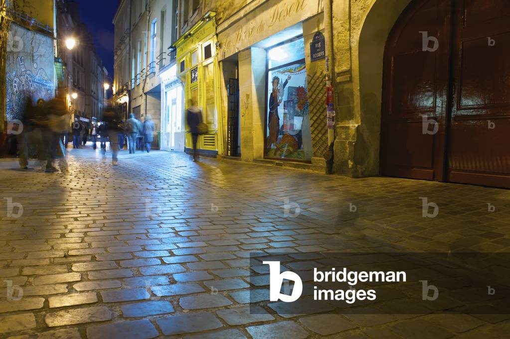 Pedestrians on a walkway outside retail buildings at nighttime, Paris, France (photo)