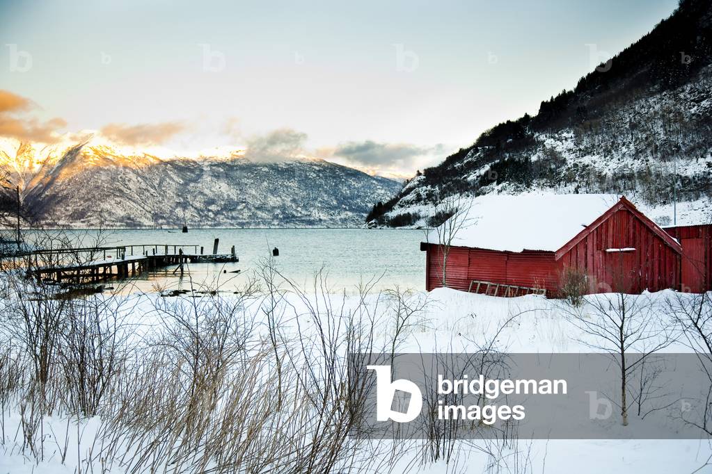 Traditonal red wooden building in the village, Fjord and mountains, with sun setting over the mountains, Ortnevik, Sognefjord, Norway (photo)