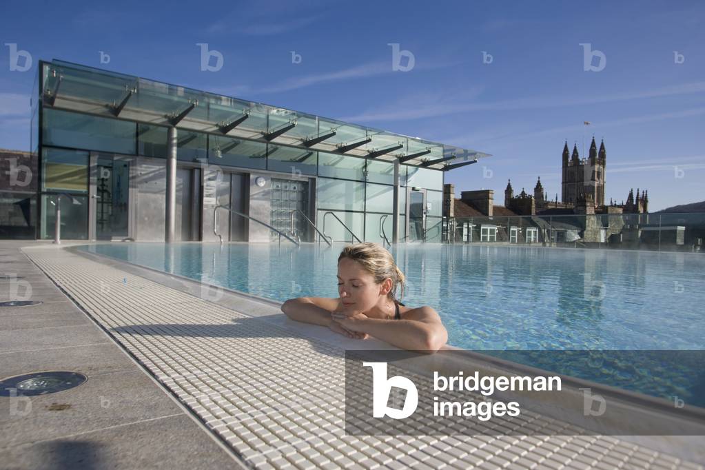 UK, England, Bath Abbey in Background, Bath, Young Woman Relaxing in Roof Top Pool at Thermae Bath Spa (photo)