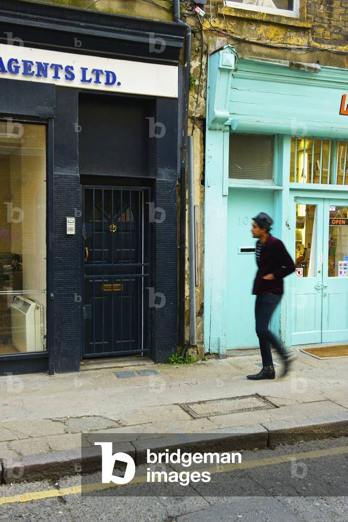 Pedestrian walking along street beside retail buildings, Brick Lane, London, England, UK  (photo)