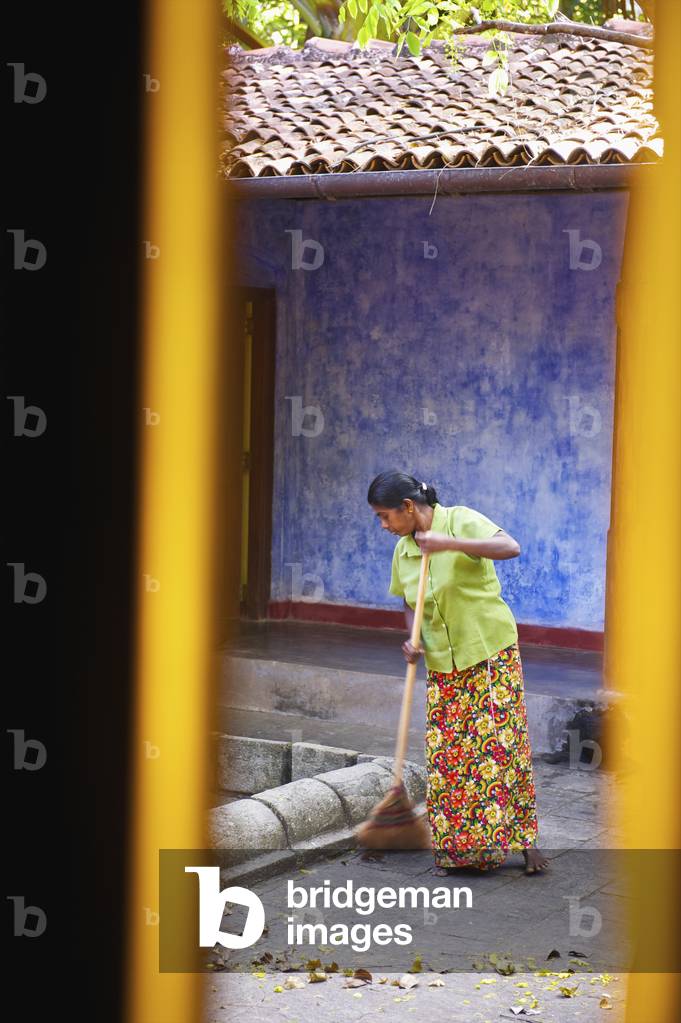 A woman sweeping a walkway, Ulpotha, Embogama, Sri Lanka (photo)