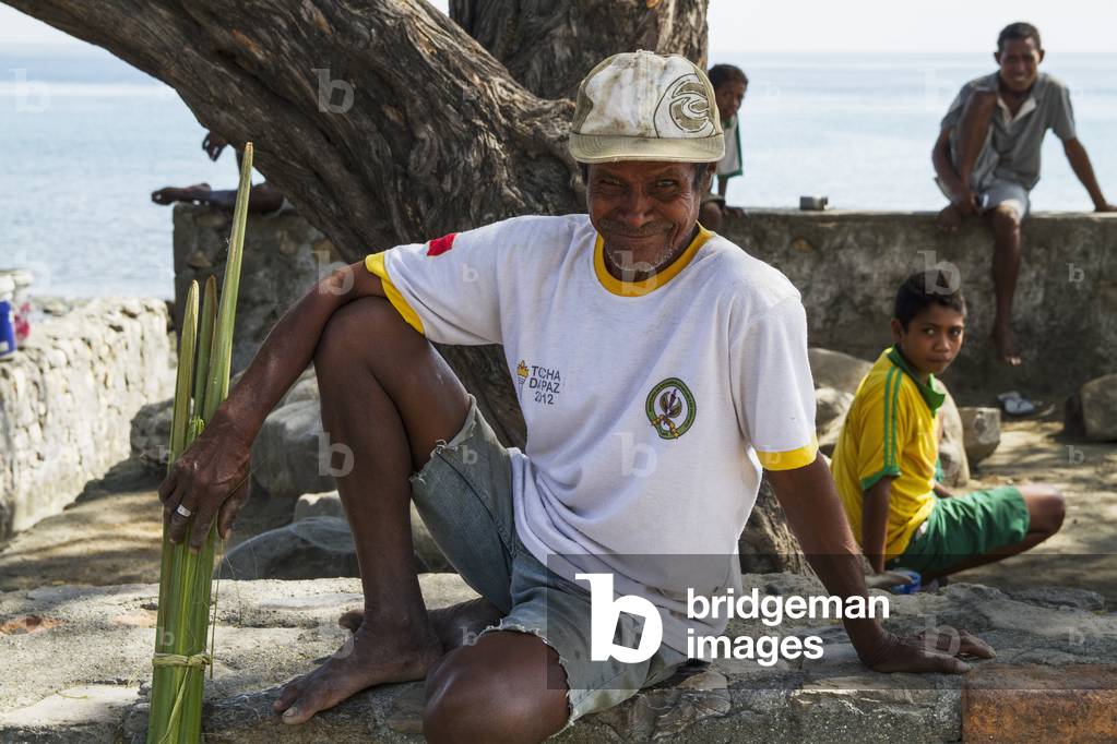 Man sitting on a stone ledge at the beach, Manatuto, East Timor (photo)