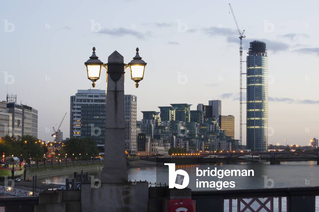 Lamp post illuminated at dusk and buildings along the waterfront, London, England, UK  (photo)