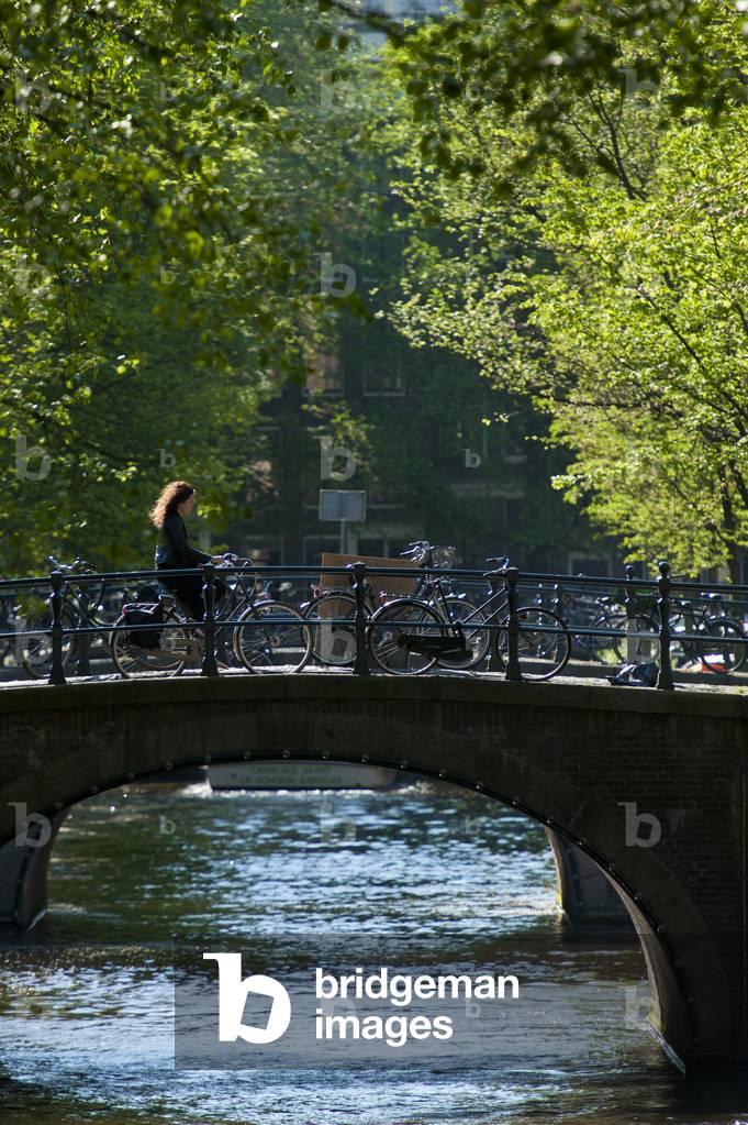 Woman on bicycle crossing bridge early in the morning, Amsterdam, Holland (photo)