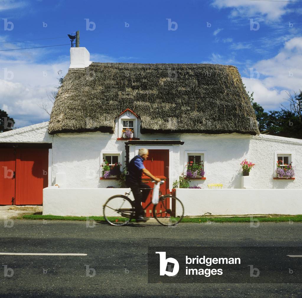 Side Profile Of A Man Riding A Bicycle In Front Of A Cottage, Mooncoin, County Kilkenny, Republic Of Ireland (photo)