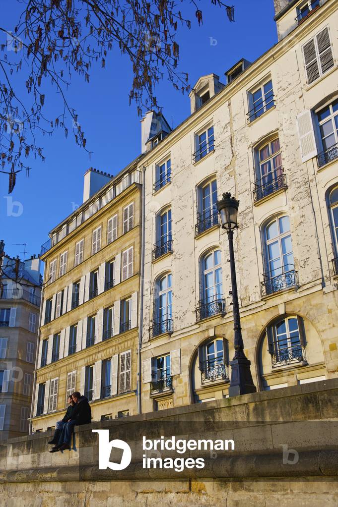 A couple sit together on a wall beside a lamp post in front of a residential building, Paris, France (photo)