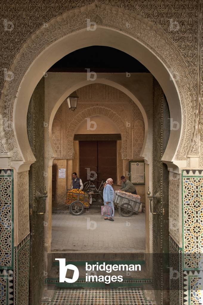 Morocco, Woman walking past orange and egg sellers outside entrance to Medersa Bou Inania, Fez (photo)