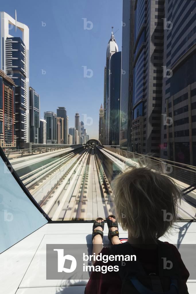 Young boy sitting at the front of metro train as it travels through the business district of Dubai, Dubai, United Arab Emirates (photo)