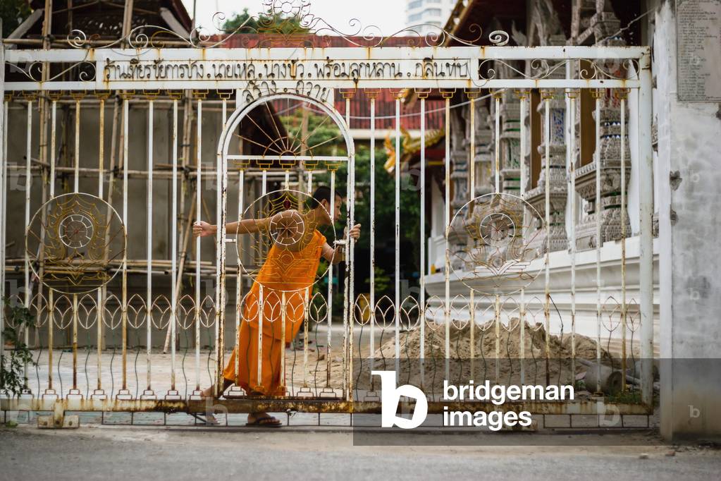 Buddhist monk opening metal gate, Chiang Mai, Thailand (photo)