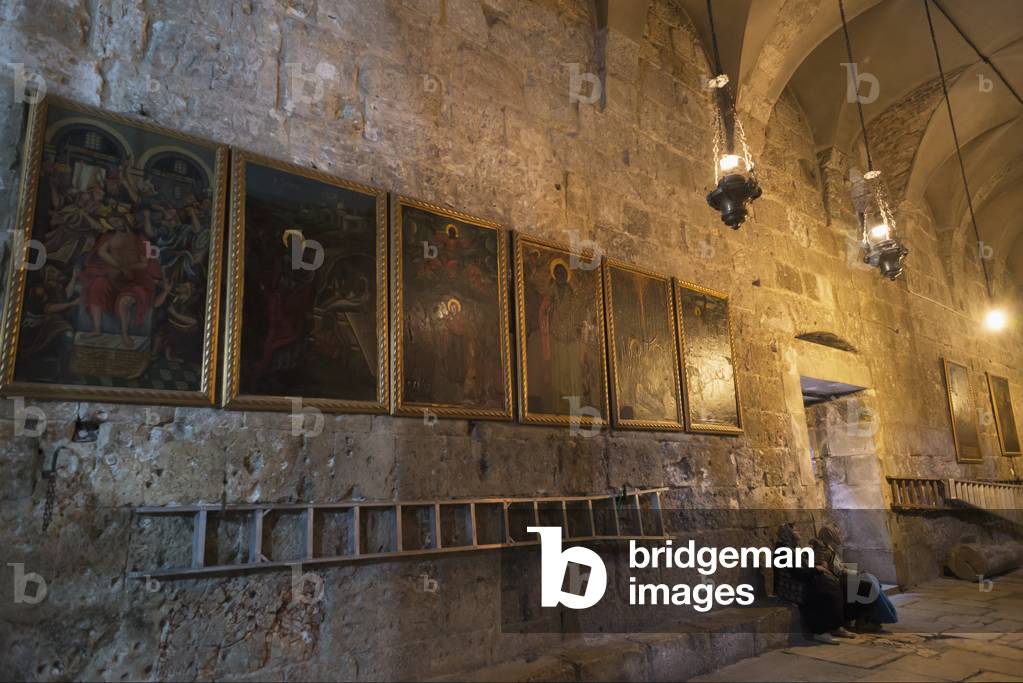 Israel, Jerusalem Old City, Church of Holy Sepulcher, Jerusalem, Two female pilgrims sitting under paintings of holy scenes (photo)