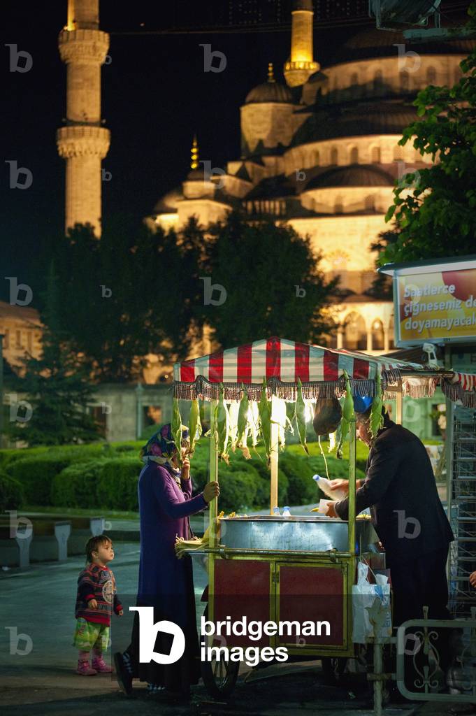 Turkey, Mother  and Child Buying From Sweet Corn Seller in Front of Sultanahmet or Blue Mosque at Night, Istanbul (photo)
