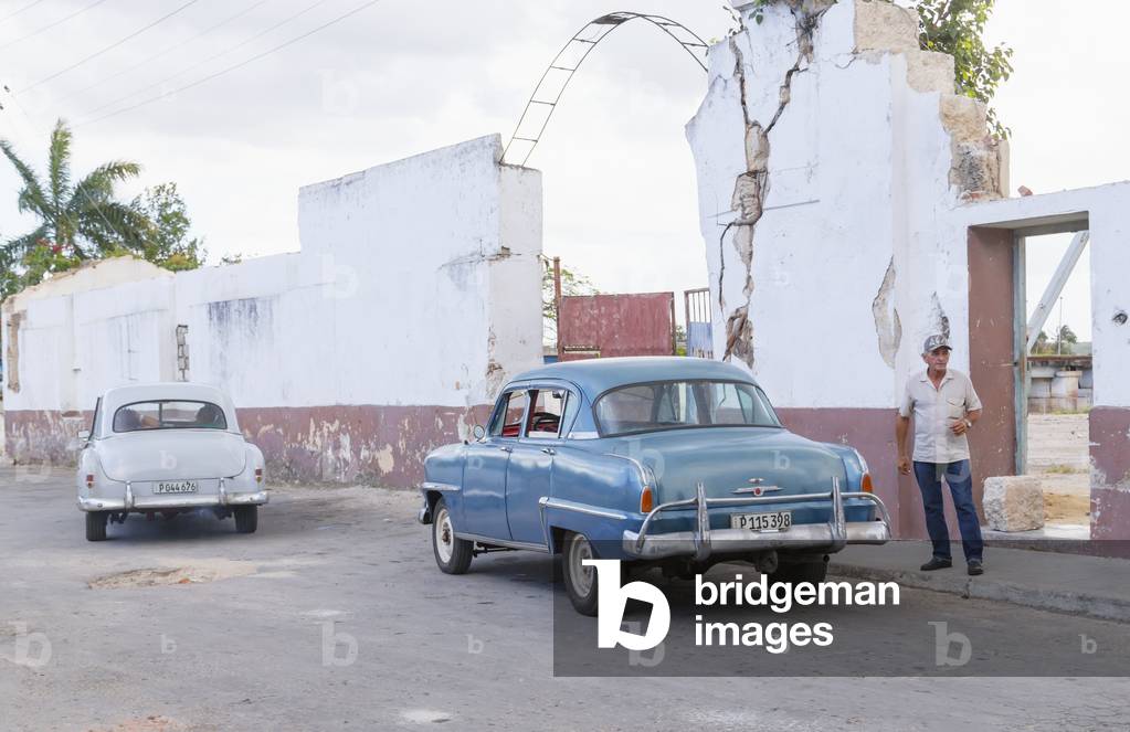 A street view of Cuba with vintage cars and a middle aged man standing on the sidewalk, Matanzas, Cuba (photo)