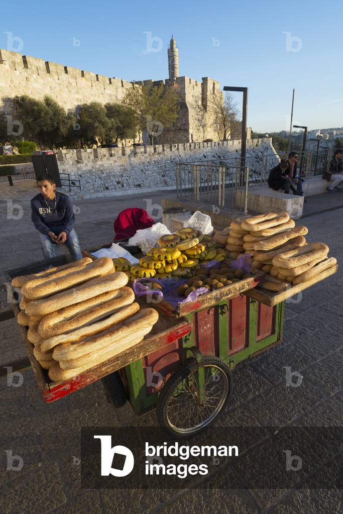 Israel, Jerusalem Old City, Youngster hawker selling bagel bread at stall with Citadel of David in background, Jerusalem (photo)