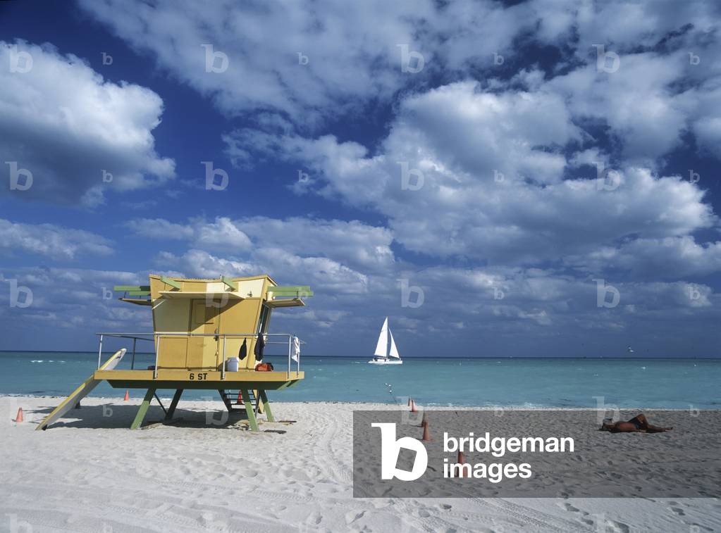 Man Sunbathing Beside Lifeguards Tower on South Beach as Yacht Goes by in the background, Miami, Florida, USA (photo)