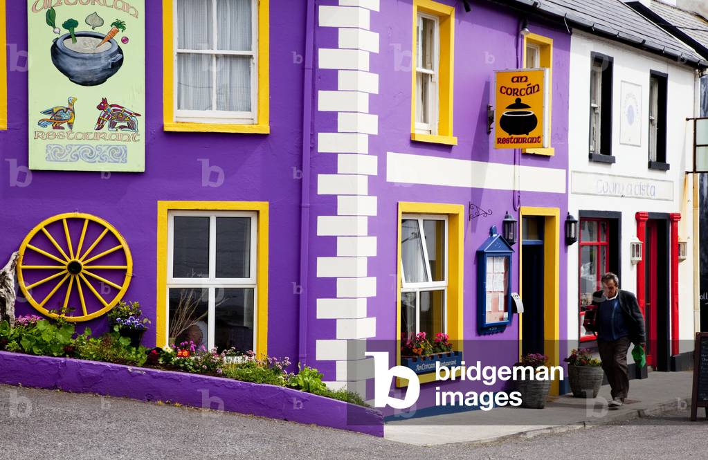A colourful shop on the corner and a pedestrian walking by; Waterville, County Kerry, Ireland (photo)