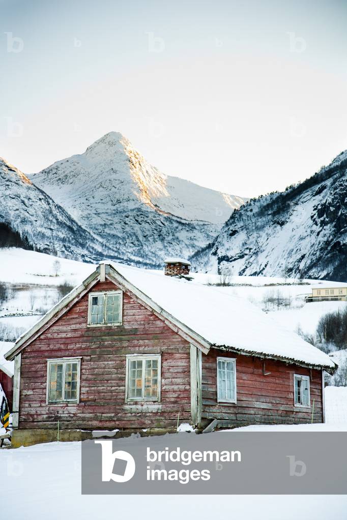 Traditional red wooden building in the village with sun setting over the mountains in the winter with snow, Ortnevik, Sognefjord, Norway (photo)
