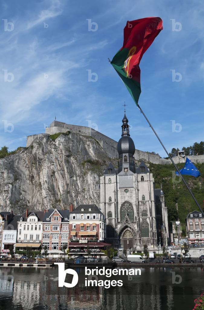 A church and other buildings along the water and flags flying, Dinant, Belgium (photo)