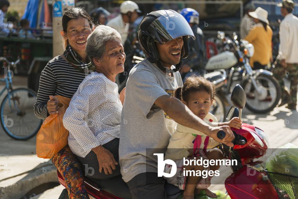 A family of four ride on a motorcycle at the Old Market, Battambang, Cambodia (photo)