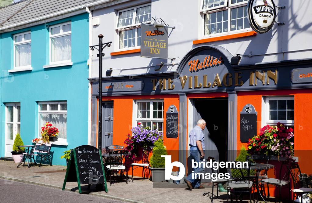 Senior man walking into Village Inn and colourful buildings along the street; Ardgroom, County Cork, Ireland (photo)