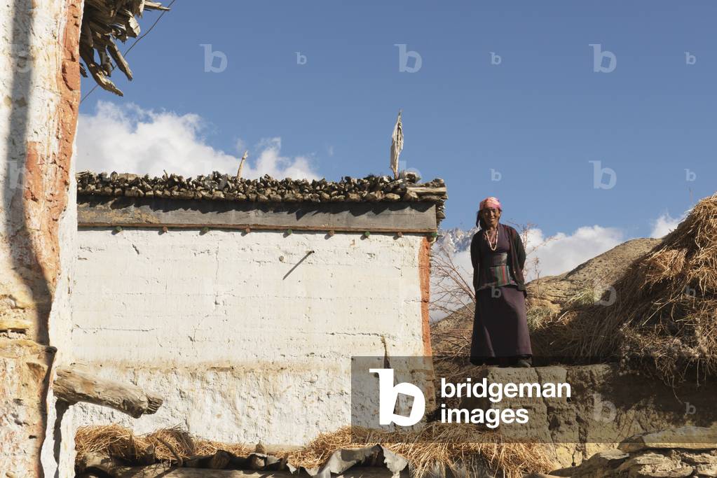 Local Woman in Traditional Dress Standing on Roof of Her House, Gyakar, Upper Mustang Valley, Nepal (photo)