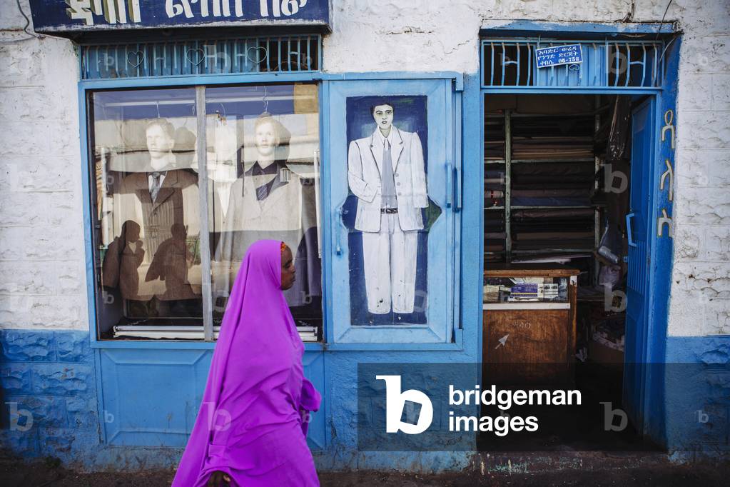Veiled woman in pink walks past a tailors shop in the old city of Harar in Eastern Ethiopia, Harar, Ethiopia (photo)