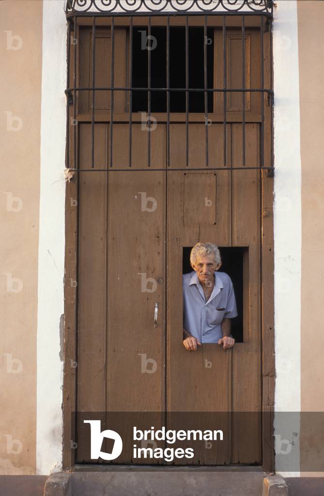 Man looking out window of wooden door, Trinidad, Cuba (photo)