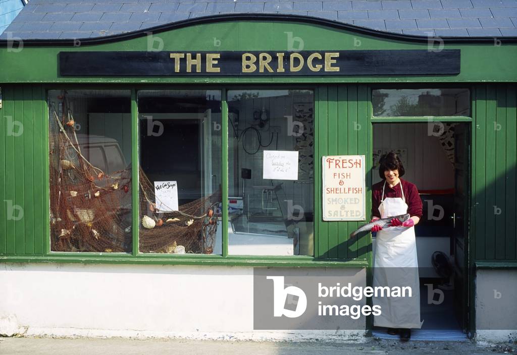 The Bridge, Skibbereen, Cork, Ireland; Woman Standing Outside Of A Fish Shop (photo)