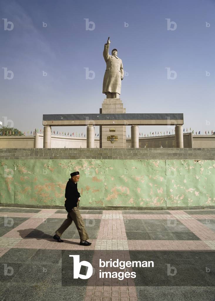 Uyghur Man Walking Under Statue of Mao (photo)