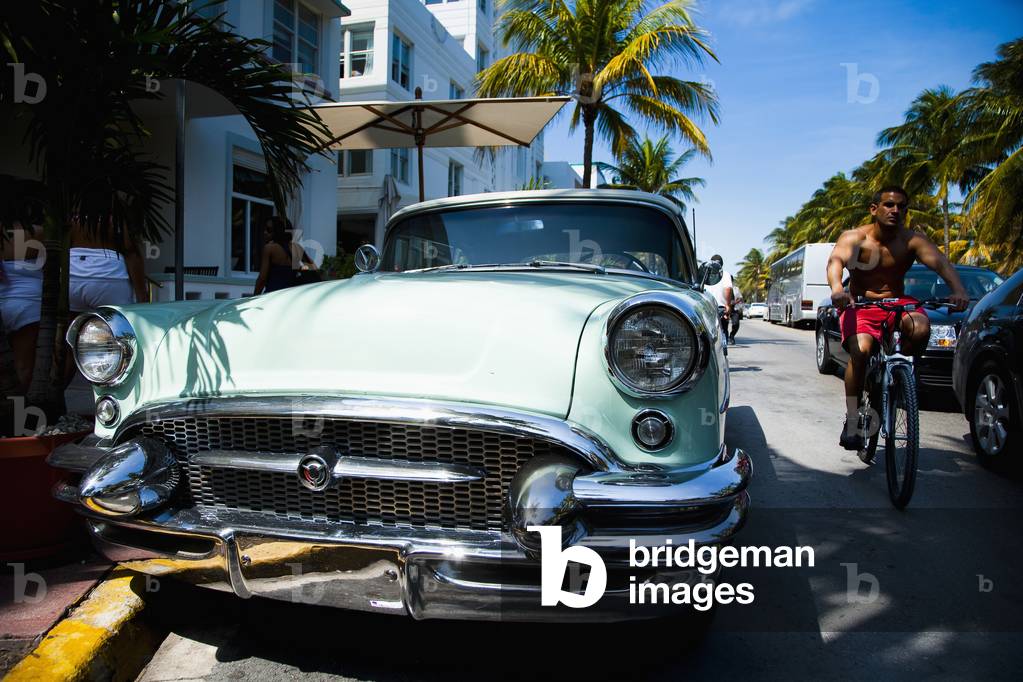 USA., Florida, Miami, Ocean Drive,South Beach, parked, Cyclist passing 1950s classic Buick car (photo)