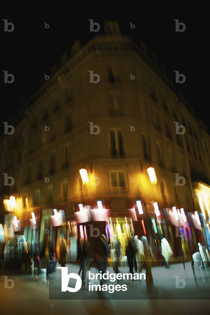 Blur of lights on a building at nighttime and pedestrians walking by, Paris, France (photo)