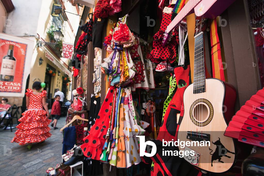 Girl in Traditional Seville Dress Passing Shop Selling Souvenirs in Old Town, Santa Cruz, Seville, Andalucia, Spain (photo)